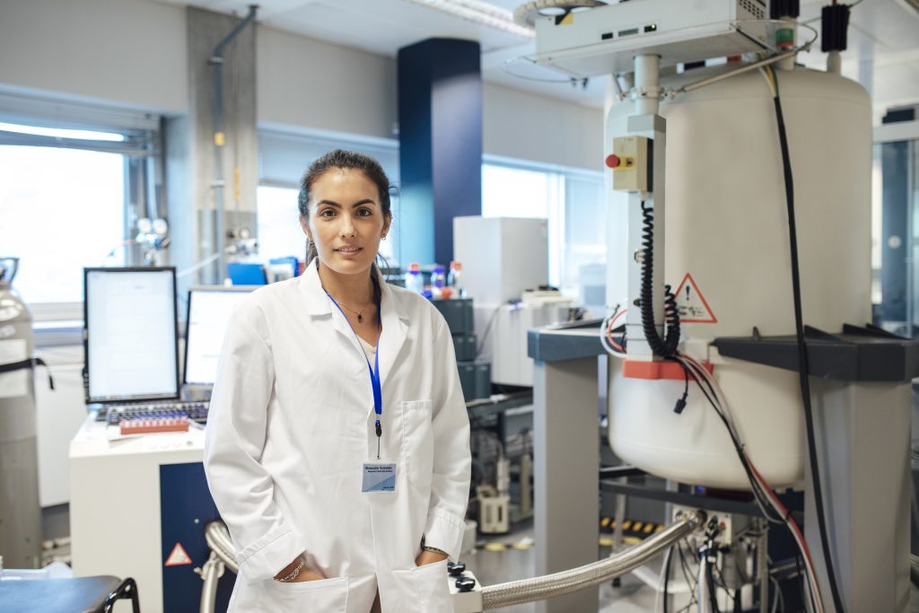A researcher standing in a lab wearing a lab coat. 