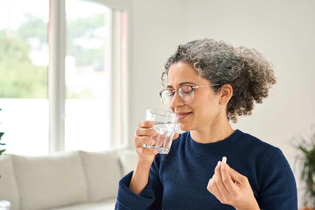 A woman taking a tablet with a glass of water.